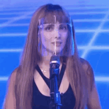 a woman wearing a face shield is singing into a microphone on a stage .