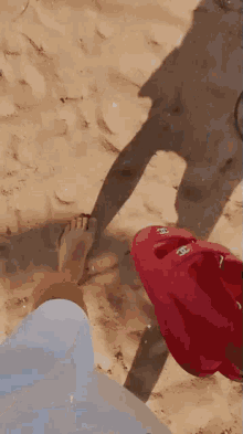 a person 's foot is on the sand next to a red kayak with the letters cc on it