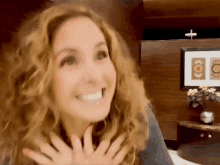 a woman with curly hair is smiling in front of a picture of a cross