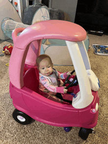 a baby is sitting in a pink cozy coupe car