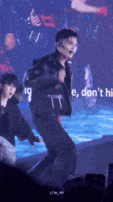 a man in a leather jacket is dancing on a stage with the words " e , don 't hi " in the background