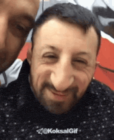 a man with a beard is smiling for the camera while another man looks on .