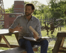 a man sits at a picnic table holding a clipboard and a piece of paper