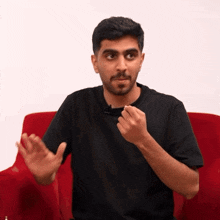 a man wearing a black shirt is sitting in a red chair
