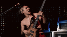 a shirtless man is playing a guitar in front of a microphone