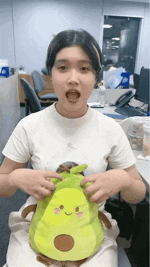 a woman is holding an avocado stuffed animal in her lap