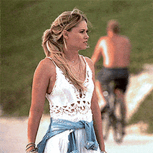 a woman in a white dress with a blue shirt around her waist is walking down a road
