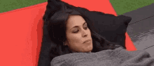 a woman is wrapped in a blanket and laying on a red cushion .