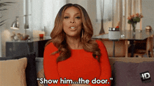 a woman in a red dress is sitting on a couch and saying show him the door