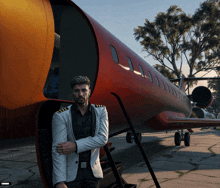 a man in a suit leans against a red airplane