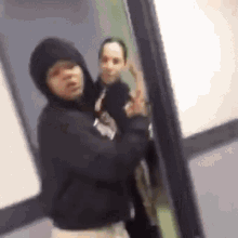 a blurry picture of a man in a hoodie standing in a hallway with another man