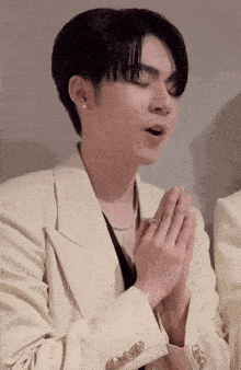 a man wearing a white jacket is praying with his hands together
