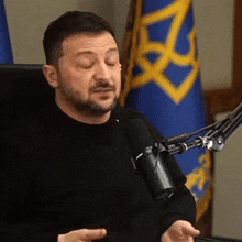 a man is sitting in front of a microphone with his eyes closed and a flag in the background .