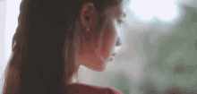 a close up of a woman 's face with a red shirt on looking out a window .