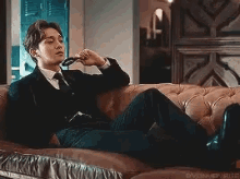 a man in a suit and tie is sitting on a couch holding a tie .