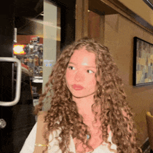 a young woman with curly hair stands in front of a door