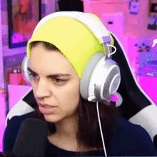 a woman wearing headphones and a yellow beanie looks at the camera