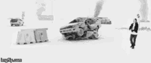 a black and white photo of a man standing in front of a burning car in the snow .