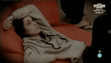 a woman is laying on a red couch with her hands on her head
