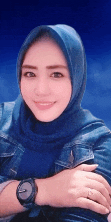 a woman wearing a blue hijab and a watch looks at the camera
