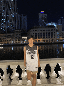 a man wearing a jersey with the number 12 on it stands in front of a body of water