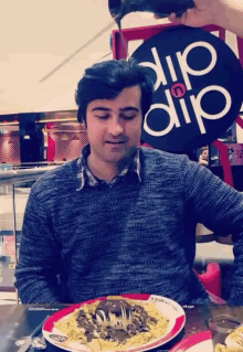 a man sits at a table with a plate of food in front of a sign that says dip