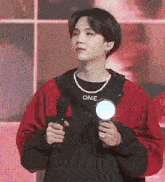 a young man in a red jacket is holding a microphone and a pearl necklace .