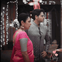 a woman in a pink saree stands next to a man in a gray shirt