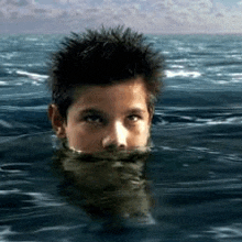 a young boy is swimming in the ocean with his head above the water .