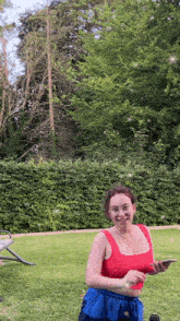 a woman in a red tank top and blue shorts is blowing bubbles in a park