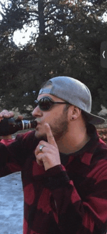 a man wearing sunglasses and a hat is drinking from a bottle of beer