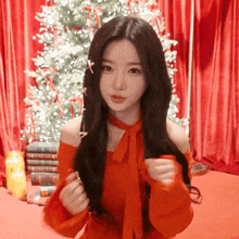 a woman in a red off the shoulder top is standing in front of a christmas tree
