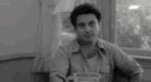 a black and white photo of a man sitting at a table with the word who behind him