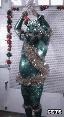 a green cat with christmas decorations and the word cets on the bottom right