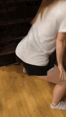 a woman in shorts is squatting on a wooden floor .