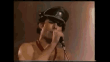 a shirtless man is singing into a microphone while wearing a leather hat .