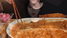 a woman is eating a plate of food with chopsticks and a bowl of pickles