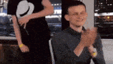 a man in a gray shirt is clapping his hands while another man stands behind him
