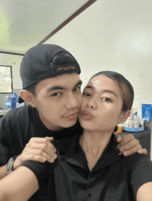 a man kissing a woman on the cheek while wearing a black hat that says tmsrns