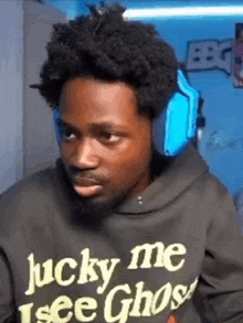 a man wearing headphones and a lucky me i see ghost hoodie is making a funny face .