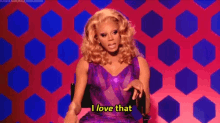 a drag queen in a purple dress is sitting in a chair and says `` i love that '' .