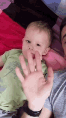 a baby laying on a bed with a man holding his hand over his mouth
