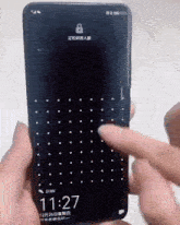 a person is holding a cell phone that says 11:27 on it
