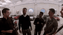 a group of men are standing in a garage talking