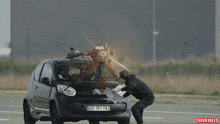 a man squats next to a car with a license plate that says dd-161-ta