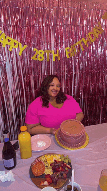 a woman in a pink shirt is sitting at a table with a cake and a sign that says happy 28th birthday