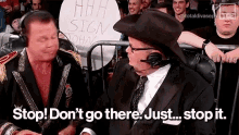 two men are sitting in front of a crowd with a sign that says stop ! don 't go there . just stop it .