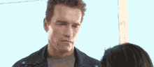 a man in a leather jacket looks at a woman in a grey shirt