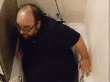 a bald man wearing glasses and a black shirt stands in a bathroom