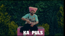 a man wearing a pink hat is sitting on a pink box with ka puls written on the bottom